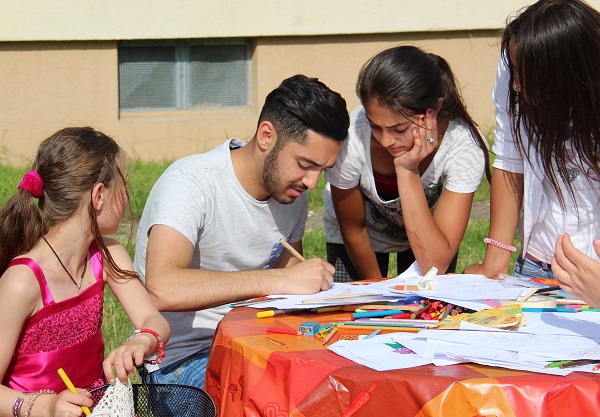 Kinder aus verschiedenen Ländern und Altergruppen sitzen zusammen am Tisch, malen und tauschen sich aus