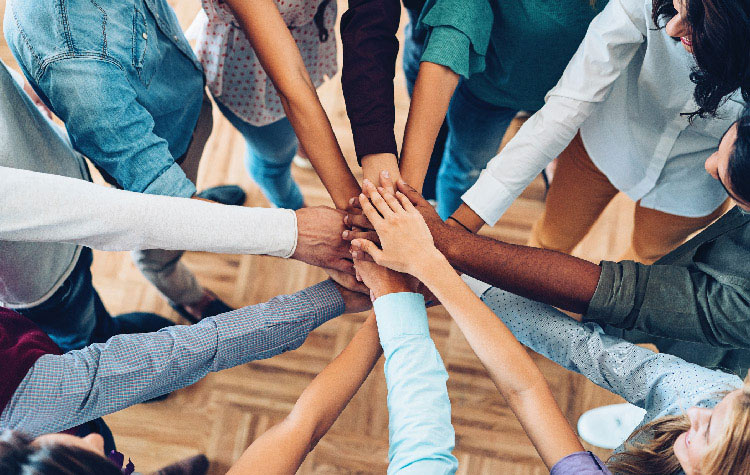 Ten employees are standing in a circle with their hands stacked together in the middle.