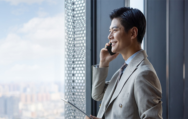 Young businessman stands in front of a large window front making a phone call