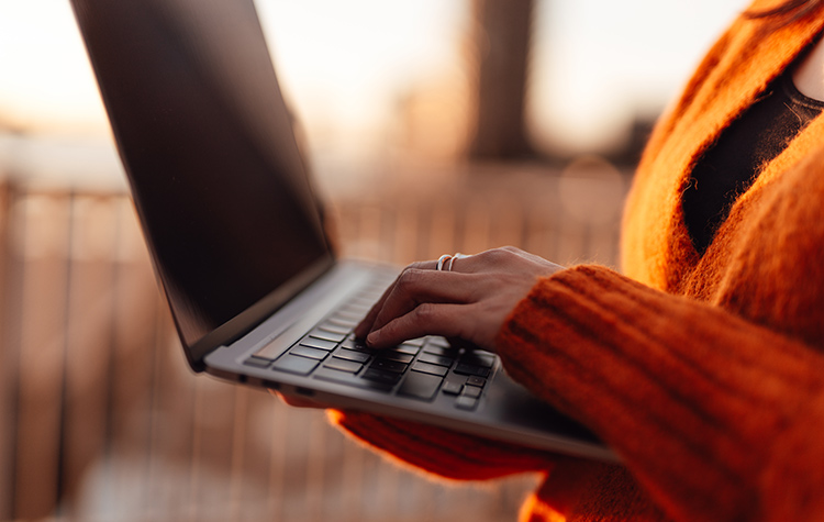 Frau hat stehend ihren aufgeklappten Laptop in beiden Händen