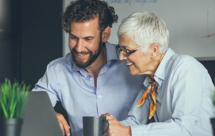 Grauhaarige Frau lacht mit einem ihrer Kollegen