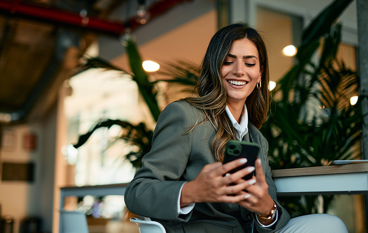 Junge Frau sitzt im Cafe und surft mit ihrem Handy auf der Karriere-Services-Webseite