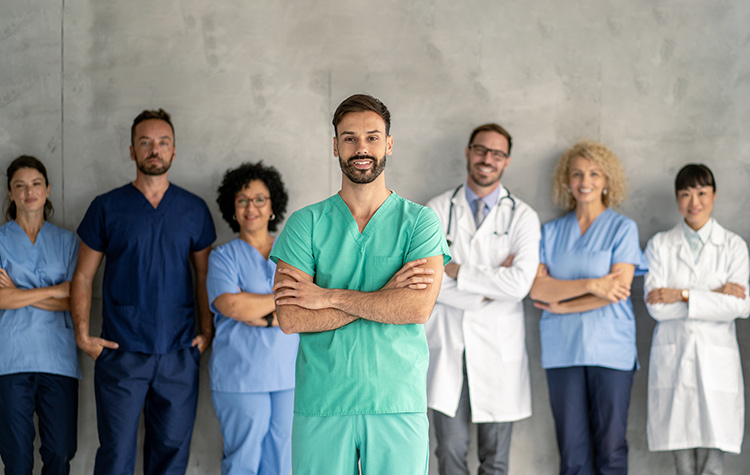 Krankenhaus-Mitarbeitende stehen lächelnd vor einer Betonwand nebeneinander