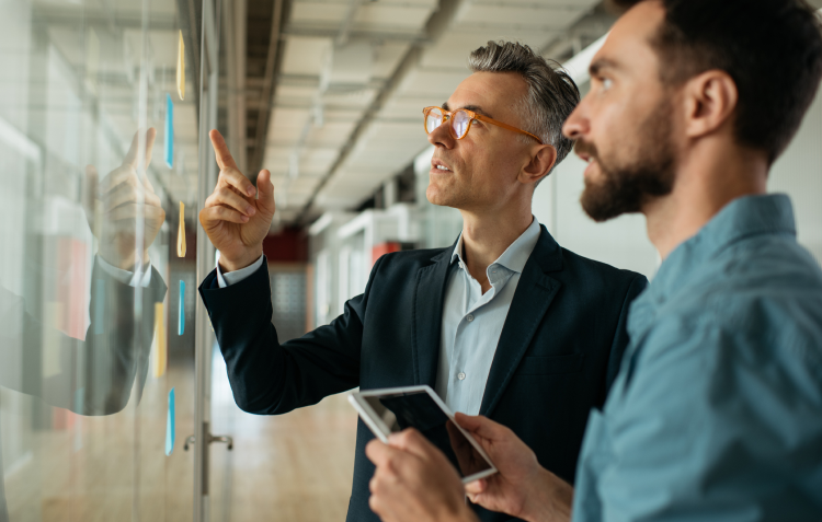 Zwei Mitarbeiter stehen vor einem Whiteboard und unterhalten sich
