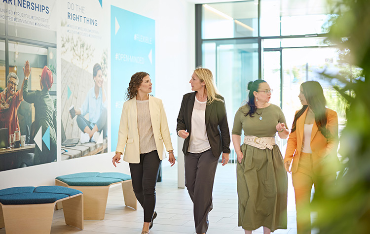 Vier Kolleginnen laufen nebeneinander durchs Foyer