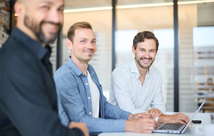 Drei Mitarbeiter lächeln in die Kamera