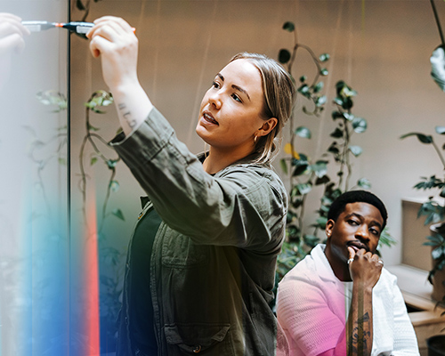 Kollege und Kollegin arbeiten mit Markern an einem Whiteboard