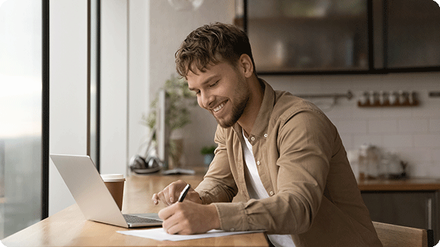 Junger Mann sitzt am Esstisch am Laptop