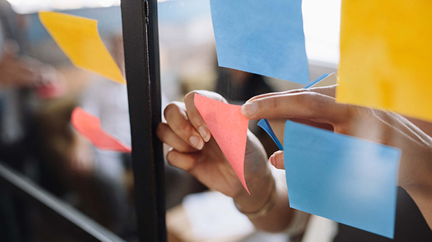 Frauenhände kleben Postits an eine Glasscheibe