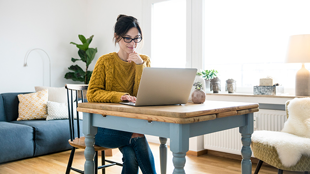 Junge Frau sitzt zu Hause am Esstisch an ihrem Laptop