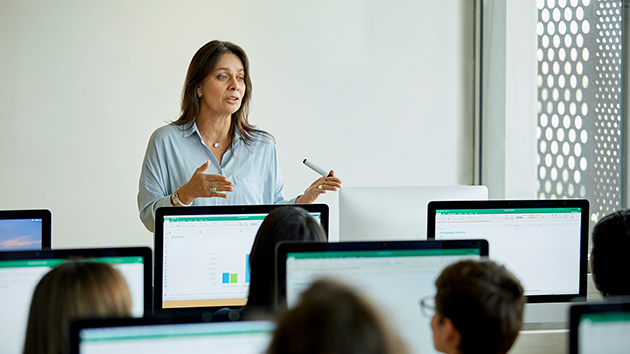 Lehrerin präsentiert/unterrichtet Klasse an PCs