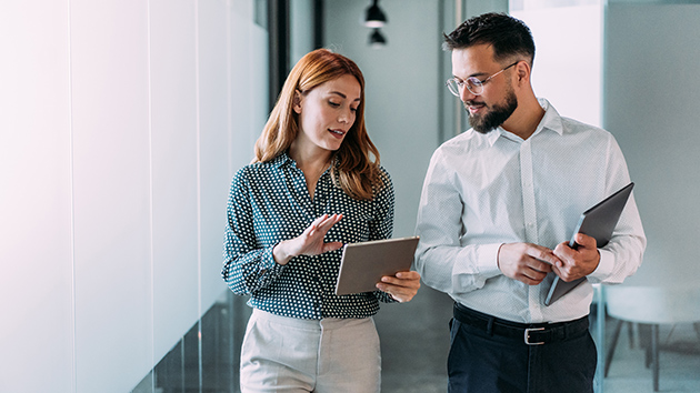 Mann und Frau laufen mit Tablets über den Flur und sprechen miteinander