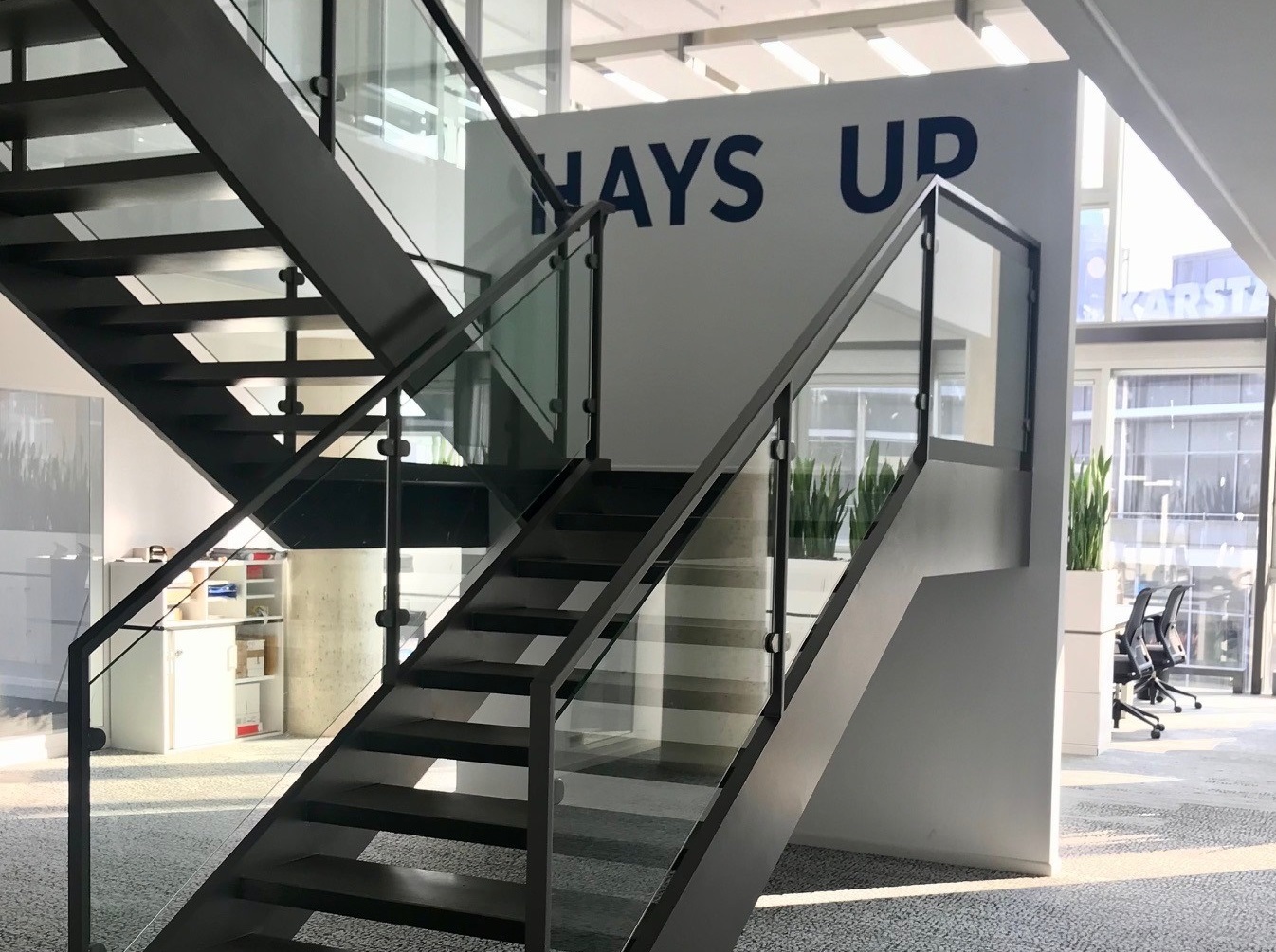 Internal view of Hays offices in Dresden: Stairway with writing: Hays Up. Background: office chairs and tables. The view out fo the window shows the city centre.